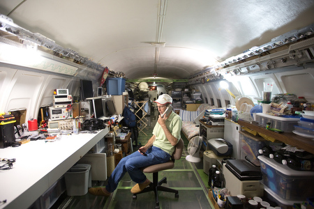 Campbell talks on the phone in the middle of his plane's cabin. The white desk at left is the workbench where Campbell, an electrical engineer, runs his business: building high-current milliohm meters used primarily for testing medical technology equipment for shock hazards.