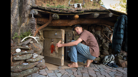 Dan Price crouches to enter what he calls his 'Hobbit hole' house, which he built into a hillside in the small town of Joseph in northeast Oregon. Using scrap wood, he spent $75 to build it; most of that paid for fasteners and sealants. The living space is eight feet across and shaped like a circle with a four-feet-high sloped ceiling. 'The things I need are food, clothing, shelter,' said Price, who lives on about $5,000 a year. Adopting a life of radical simplicity, he said, 'stopped all of my worrying about money and jobs.'